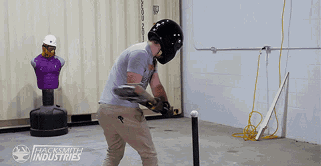 a man wearing a helmet is holding a guitar in a room with hacksmith industries written on the wall