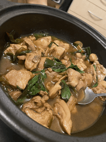 a bowl of chicken stew with spinach and mushrooms with a spoon in it