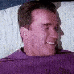 a man in a purple shirt is smiling while laying in bed .