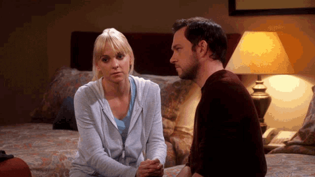 a man and a woman sit on a bed with a lamp in the background