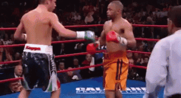 two men are fighting in a boxing ring with a referee in the background .