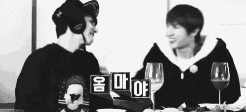 two men are sitting at a table with glasses of wine .