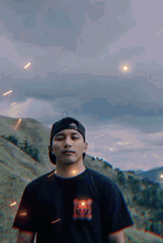 a man wearing a black shirt with a tiger on it is standing on a hill