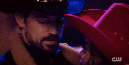 a woman in a cowboy hat is hugging a man in a cw logo