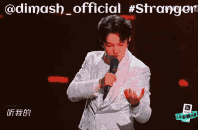 a man in a white suit is singing into a microphone with the words @dimash_official #stranger behind him