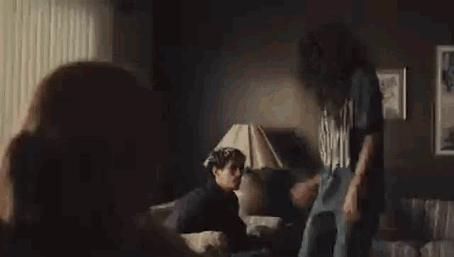 a man and woman are dancing in a living room while a woman sits on a couch .