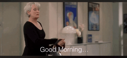 a woman in a black dress says good morning in a room