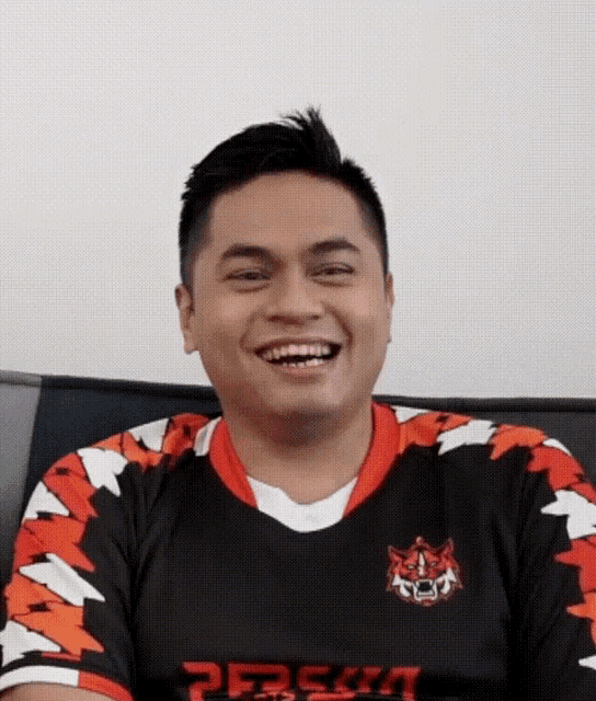 a man wearing a jersey with a tiger on it is laughing while sitting on a couch .