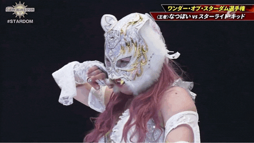 a woman wearing a tiger mask and gloves stands in front of a sign that says #stardom