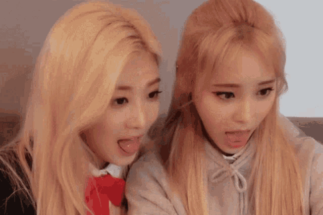 two blonde girls sticking their tongues out at each other .