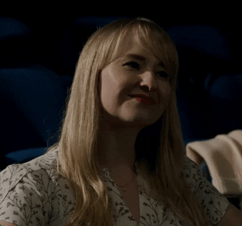a woman in a white floral shirt is sitting in a dark room