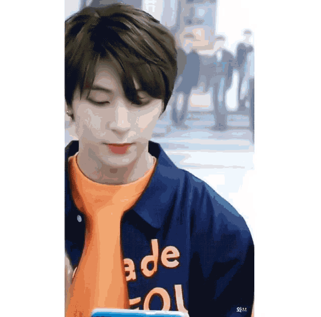 a young man wearing a blue jacket and an orange shirt with the word ade on it