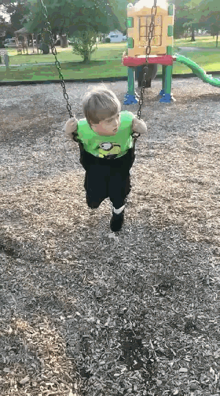 a little boy in a green shirt is swinging on a chain