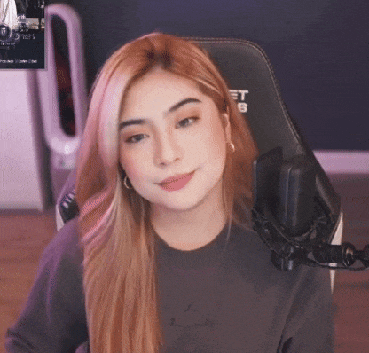 a woman is sitting in a gaming chair with a microphone and smiling