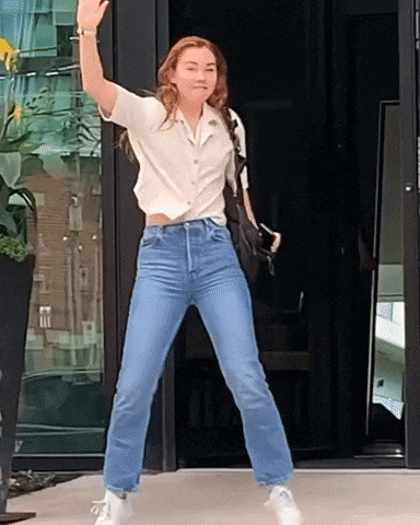 a woman in jeans and a white shirt is dancing in front of a door