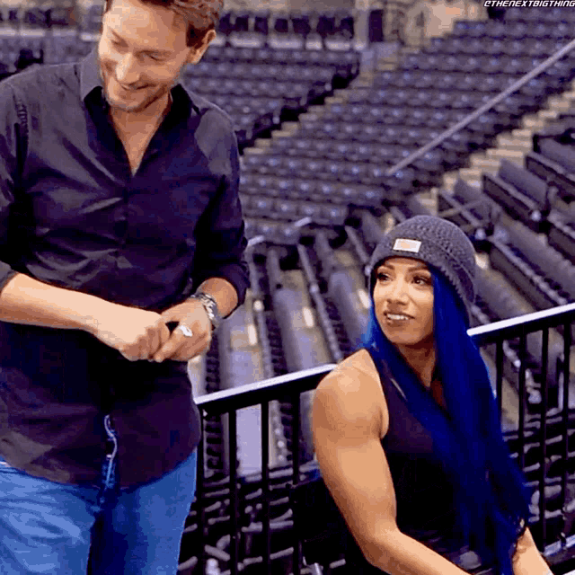 a woman with blue hair is sitting next to a man who is smiling
