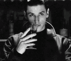 a black and white photo of a young man drinking a glass of wine .