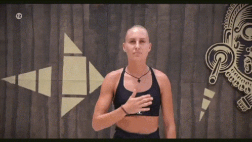 a woman in a black sports bra is standing in front of a wooden wall with her hands on her chest .