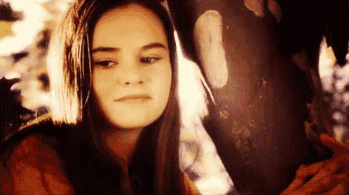 a young woman with long hair is standing next to a tree trunk .
