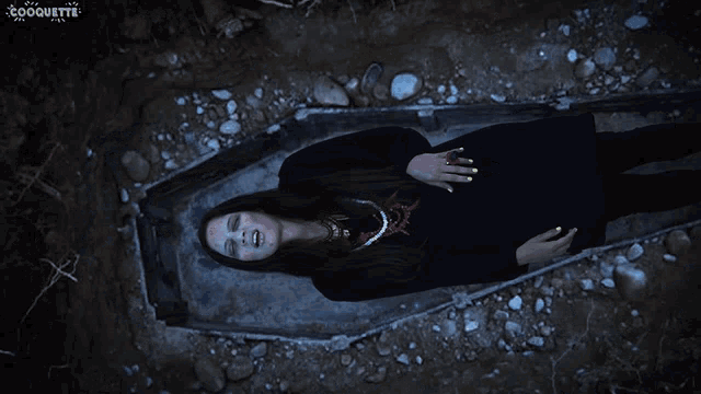 a woman in a black dress is laying in a coffin with the word coquette on the bottom right