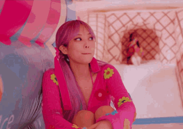 a woman with pink hair is sitting on a couch wearing a pink sweater and making a funny face .
