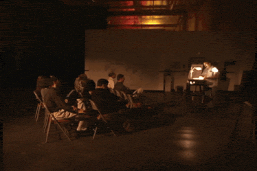 a group of people are gathered in a dark room watching a robot being built