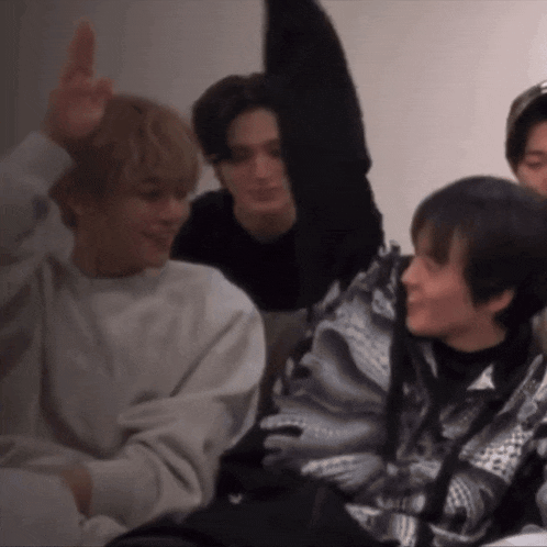 a group of young men are sitting on a couch and one of them is pointing upwards