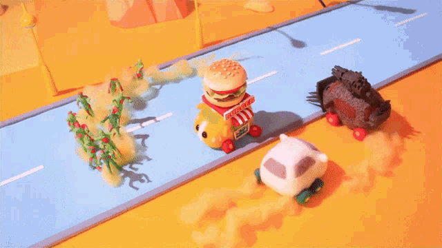 a toy car with a hamburger on top of it is driving down a road