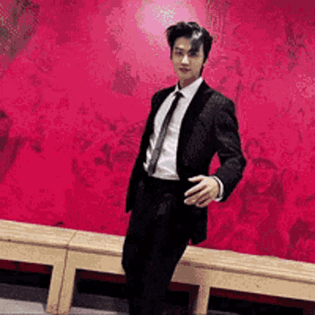 a man in a suit and tie is standing in front of a red wall .