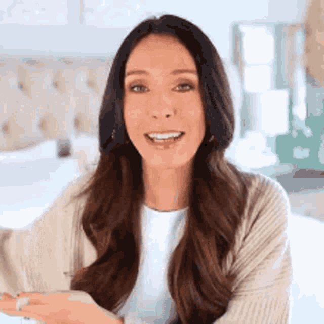a woman with long dark hair is wearing a white shirt and a beige sweater .