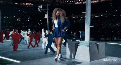 a woman in a blue skirt is dancing in front of a crowd with the word music on the bottom