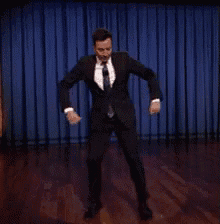 a man in a suit and tie is dancing on a stage in front of a blue curtain .