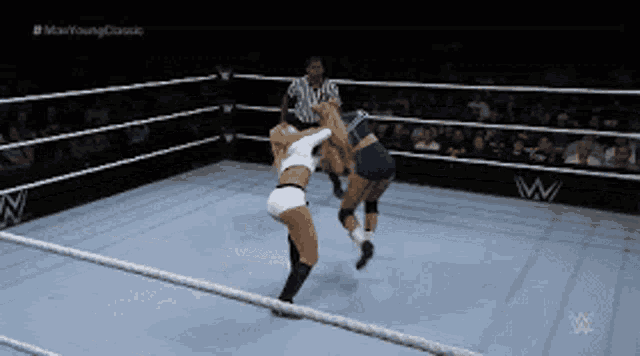 two women are wrestling in a ring with a referee in the background