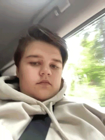 a young man wearing a hoodie and tie is sitting in a car looking out the window .