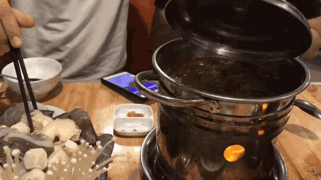 a person is holding chopsticks in front of a pot of food