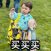 a little boy is holding a stuffed animal and a bag in a field .
