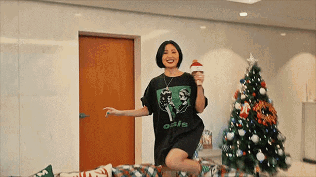 a woman wearing a t-shirt that says oasis is kneeling down in front of a christmas tree .