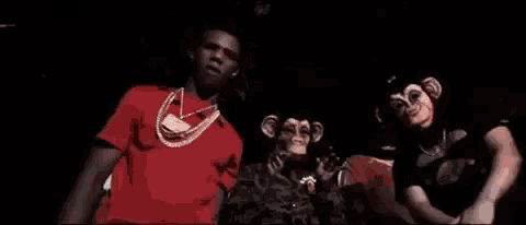 a man in a red shirt is standing next to two men in monkey masks .