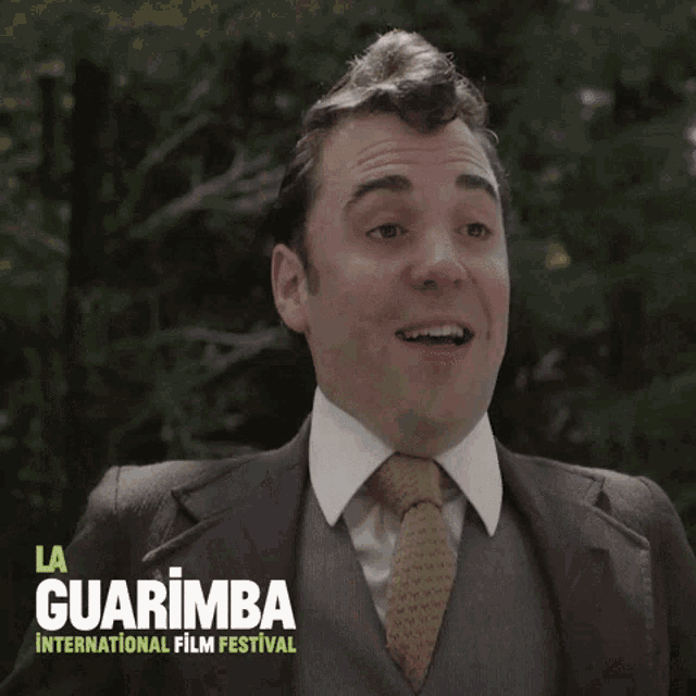 a man in a suit and tie is holding two bottles of wine with the words la guarimba international film festival behind him