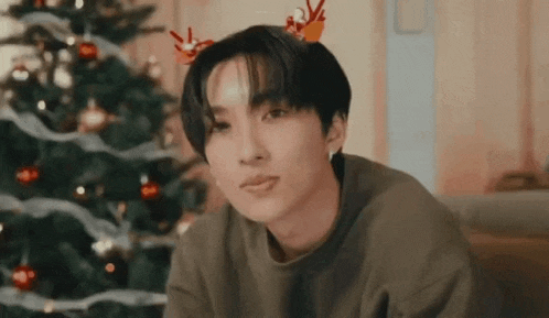 a young man wearing a reindeer antlers sitting in front of a christmas tree .