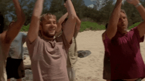 a group of men are standing on a beach with their arms in the air .