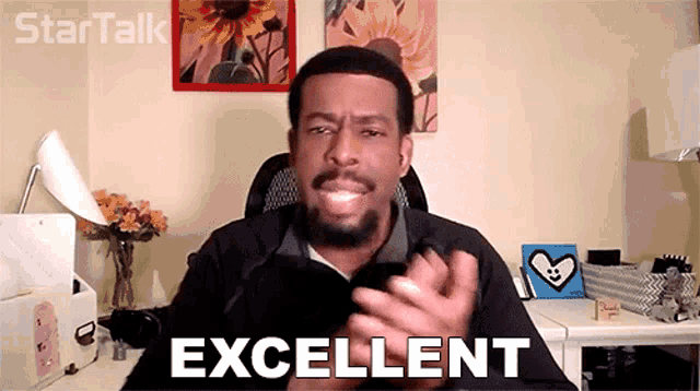 a man applauds in front of a desk that says excellent on it