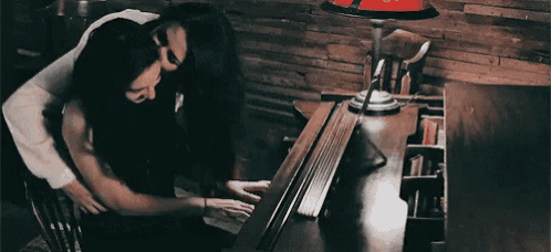 a man is hugging a woman while she plays the piano .