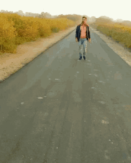 a man wearing a pink shirt and a blue jacket walks down a road