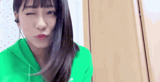 a woman in a green hoodie is making a funny face with her eyes closed .