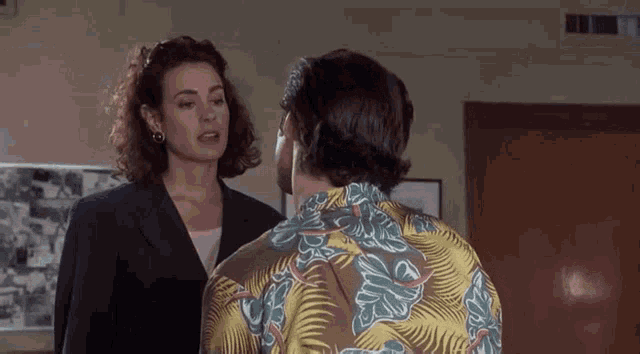 a man and a woman are talking to each other in a room . the man is wearing a hawaiian shirt .
