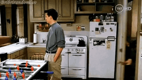 a man is standing in a kitchen next to a refrigerator and a stove ..