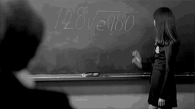 a girl is standing in front of a blackboard with the number 128 written on it .