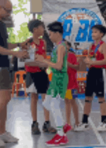 a group of young boys are standing on a basketball court holding medals and trophies .