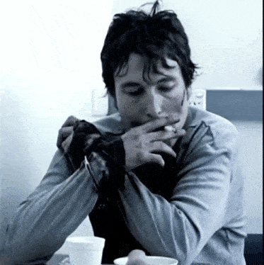a man sitting at a table smoking a cigarette and covering his mouth with his hand